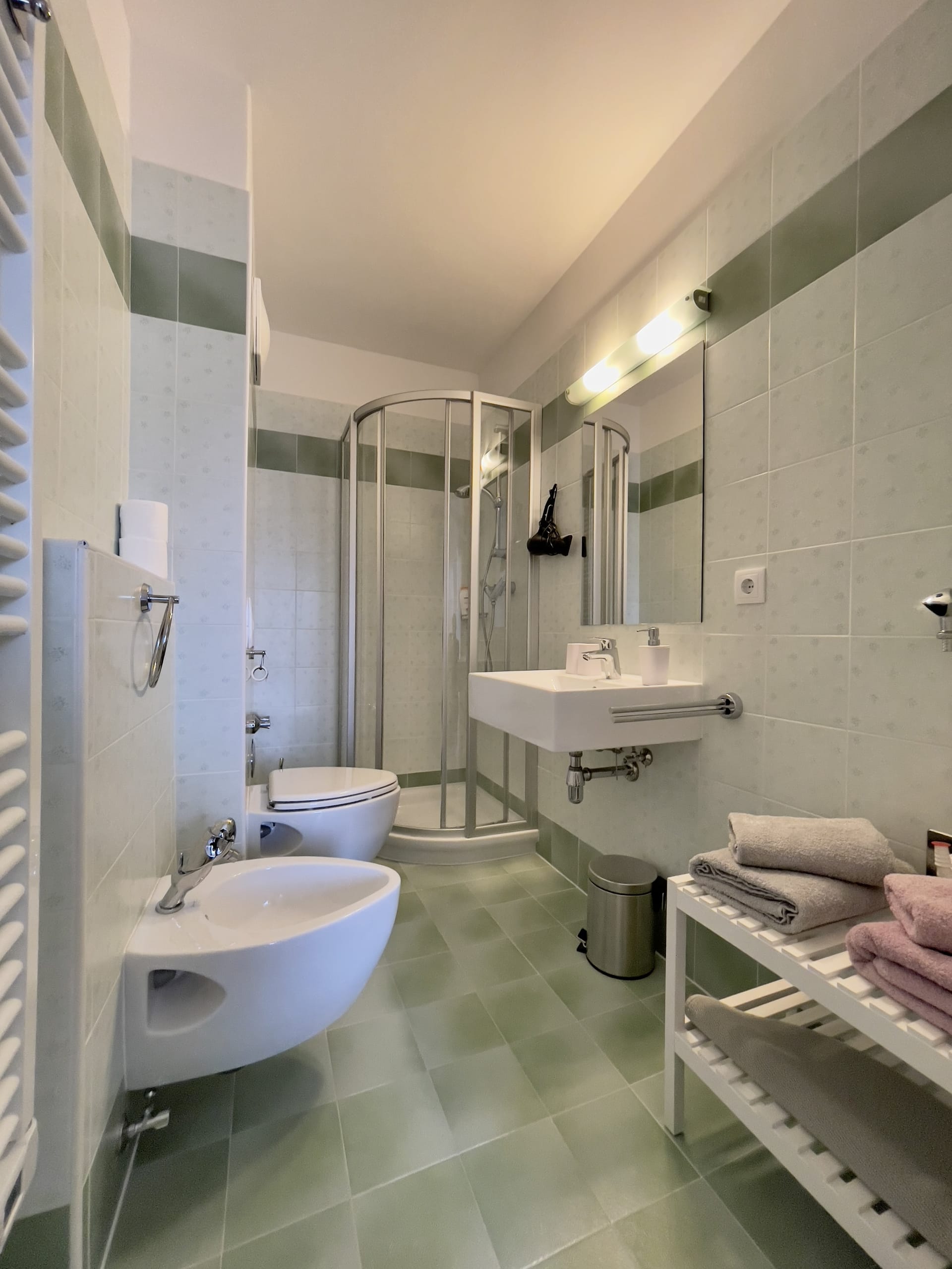 The second bathroom, with green tile, a corner shower, bidet, and sink.