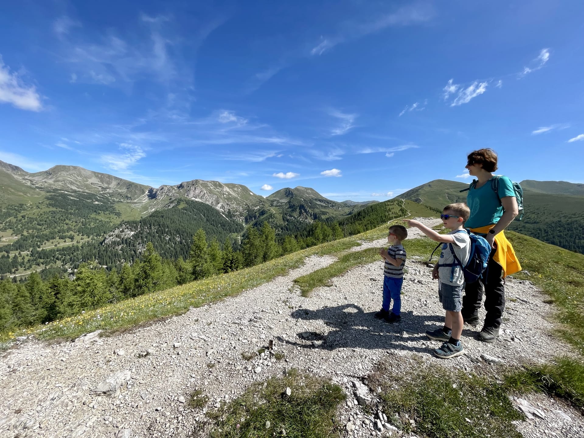 A family on an alpine ridge in summer, mountains opening up in the distance.