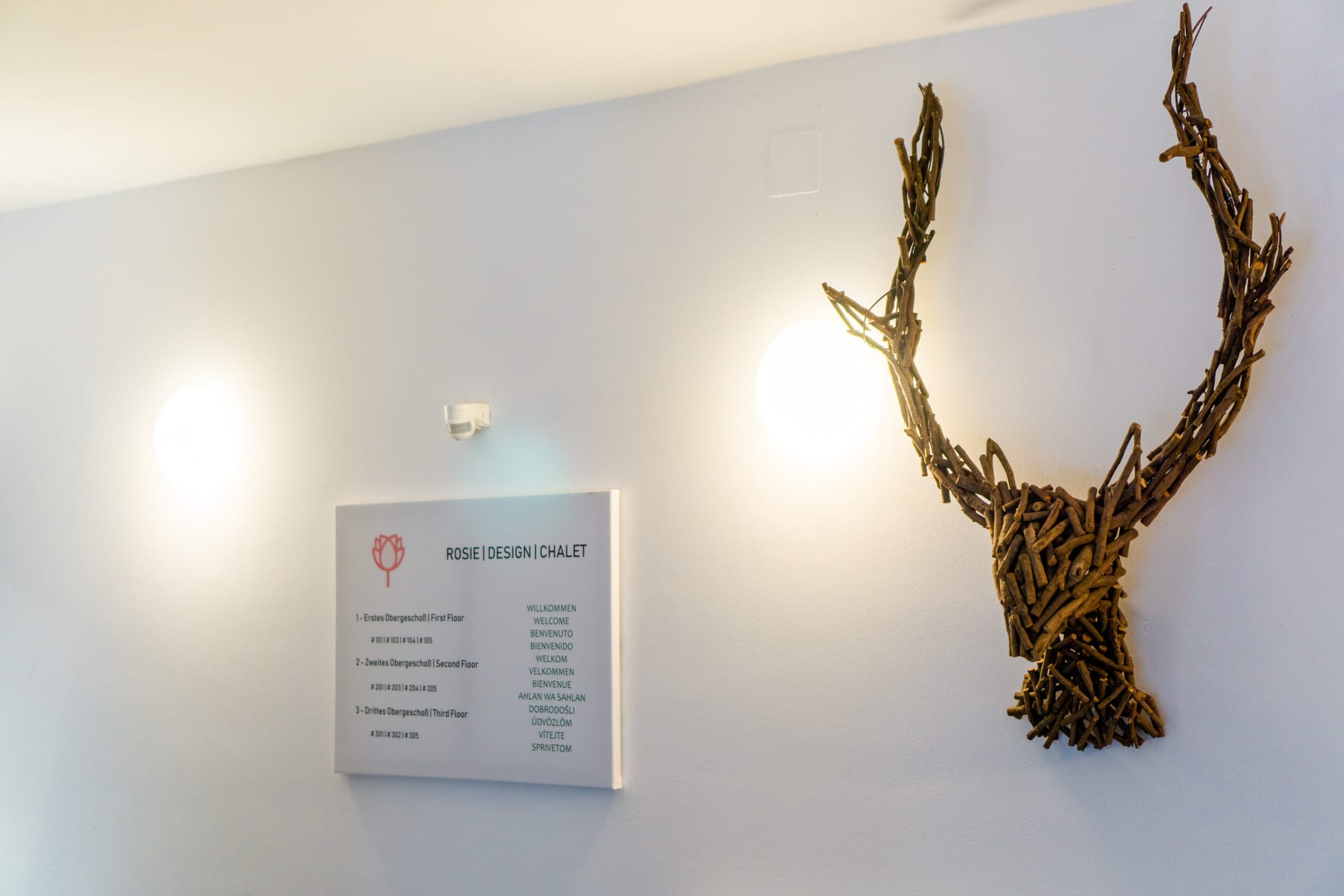 The building lobby with a Rosie Design Chalet sign, a wooden stag, and a welcome plate in many languages.